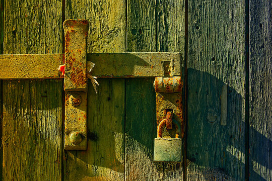 Old rusty padlock on weathered wooden door illuminated by afternoon sunlight