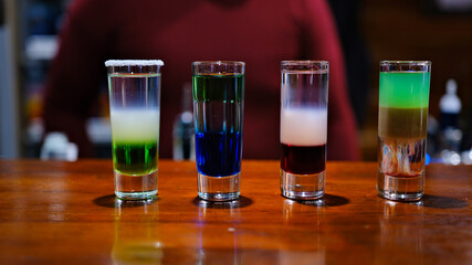 array shot glasses filled with vibrant and colorful drinks sits on a sleek bar counter. various hues reflect light and create an energetic atmosphere, perfect for a night out. 