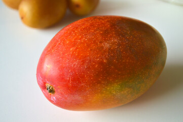 Fresh ripe mango with colorful gradient skin and citrus fruits on white background