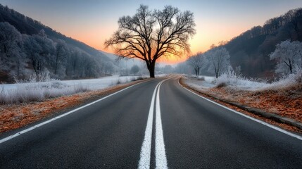 Fototapeta premium quiet road stretches through a serene winter landscape. sun sets behind frost-covered hills, casting warm colors in the sky, while a solitary tree stands tall amidst the chill