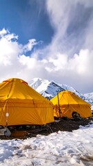 Two yellow tents on a snowy ground with a mountain backdrop