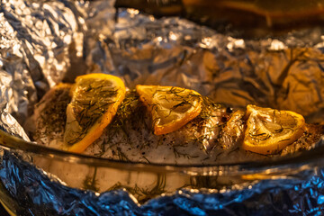 Baked in the oven in foil with spices, herbs and lemon in a baking dish, top view. Fresh baked walleye fish in foil for baking with vegetables, lemon and spices close-up. Pike-perch baked in foil. 