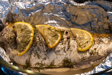 Baked in the oven in foil with spices, herbs and lemon in a baking dish, top view. Fresh baked walleye fish in foil for baking with vegetables, lemon and spices close-up. Pike-perch baked in foil. 