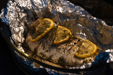 Baked in the oven in foil with spices, herbs and lemon in a baking dish, top view. Fresh baked walleye fish in foil for baking with vegetables, lemon and spices close-up. Pike-perch baked in foil. 