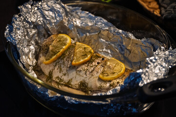 Baked in the oven in foil with spices, herbs and lemon in a baking dish, top view. Fresh baked walleye fish in foil for baking with vegetables, lemon and spices close-up. Pike-perch baked in foil. 