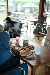Woman in hijab enjoying delicious meal at bright outdoor cafe, savoring the moment with friends and family during a relaxing weekend getaway