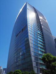 Obraz premium Modern glass skyscraper with curved façade reflecting sunlight and blue sky 