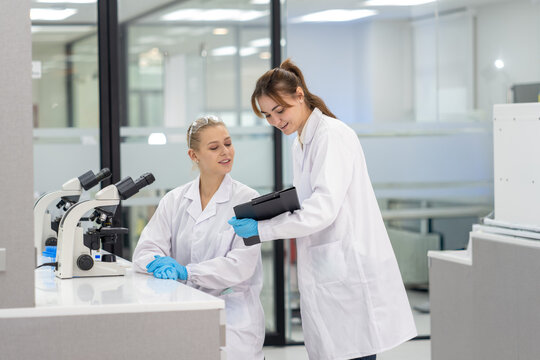 Two scientists in a modern laboratory working with a microscope and discussing findings - Powered by Adobe