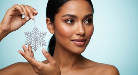Woman with glowing skin holding a silver snowflake ornament. Winter beauty and skincare concept for the christmas holiday season