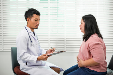 Fototapeta premium The doctor will take a medical history and assess the Asian woman's abdominal pain and discuss diagnosis and management of gastrointestinal problems, excess fat, obesity, or other health problems.