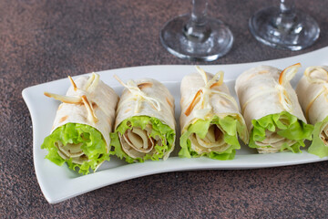 Appetizer from pita bread with ham, cheese and lettuce on white plate on brown background
