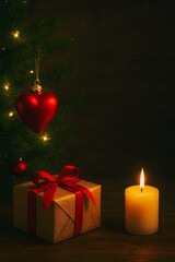 A red heart rests by a burning Christmas candle, a holiday decoration and light for the season