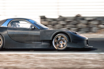 Black racing car accelerating on racetrack, generating dramatic motion blur, highlighting intense motorsport dynamics