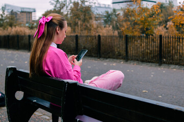 Woman in pink sitting on bench holding phone, side rear view