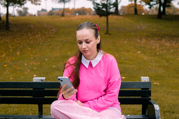 Young woman in pink reacting to message on phone in autumn park