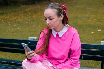 Young woman in pink reacting to message on phone in autumn park