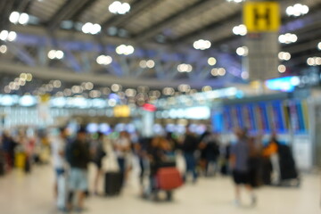 Blurred view of passengers and people at  International Airport. Travelers walking and checking flight information boards in the terminal. Busy atmosphere of people with luggage, lights, and airport.