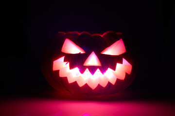 Glowing Halloween jack-o'-lantern with scary carved face illuminated by pink light in the dark
