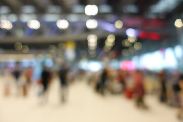 Blurred view of passengers and people at  International Airport. Travelers walking and checking flight information boards in the terminal. Busy atmosphere of people with luggage, lights, and airport.