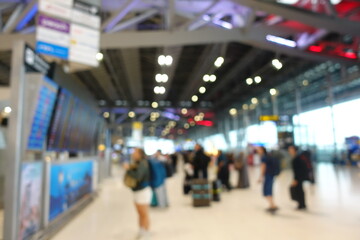 Blurred view of passengers and people at  International Airport. Travelers walking and checking flight information boards in the terminal. Busy atmosphere of people with luggage, lights, and airport.
