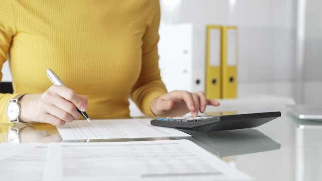 Woman doing financial paperwork, calculating budget, scrutinizing documents, and reviewing expenses with magnifying glass. Audit and taxes in business