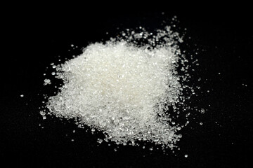 A pile of sweet granulated sugar lies on a black background.