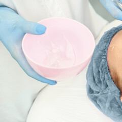 Caucasian female receiving facial treatment with gel application in spa setting by gloved therapist.