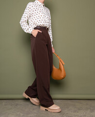 Side view of woman wearing white polka dot long-sleeve blouse and brown high-waisted trousers with...