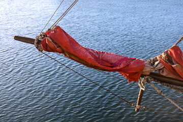 Bowsprit and furled red sail on calm water