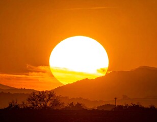 Obraz premium Golden hour captures a large sun setting behind silhouette mountains