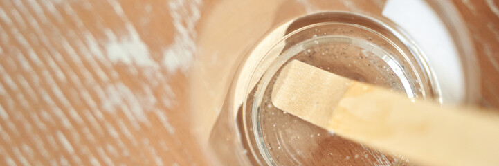 Top view of stirred epoxy resin in clear cup on wooden surface with mixing stick.