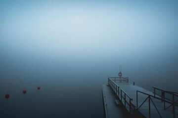 A thick fog on an ocean only revealing a boat docking pier.