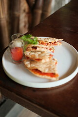 Delicious quesadillas with fresh cilantro and spicy dipping sauce served on white plate ready to eat at restaurant giving off a foodie vibe