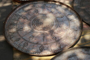 Antique copper trays and dishes with detailed engraving displayed at a flea market in Tbilisi. Warm sunlight and soft shadows create a cozy, authentic atmosphere.