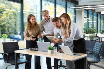 Group of young modern people in formalwear using modern technologies while working in the creative office