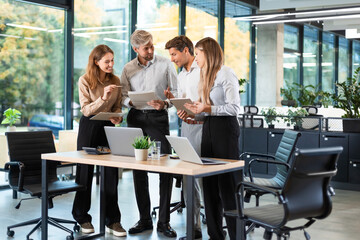 Group of business people standing together and discussing their work and projects, having a team meeting in an office.