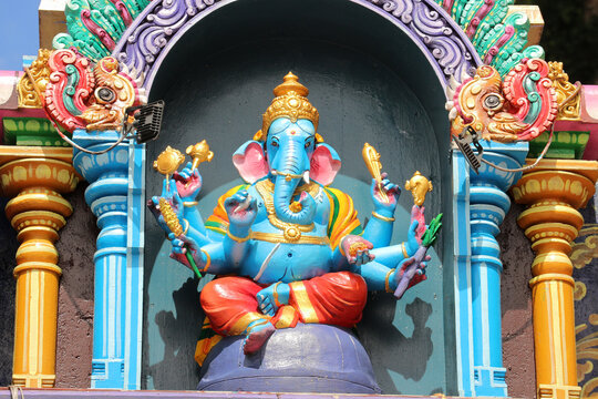 Blue multi-armed Hindu god Ganesha statue with attributes on temple exterior - Powered by Adobe