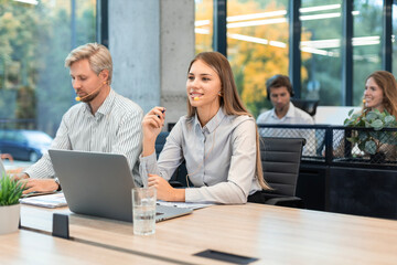 Female customer support operator with headset and smiling, with collegues at background.