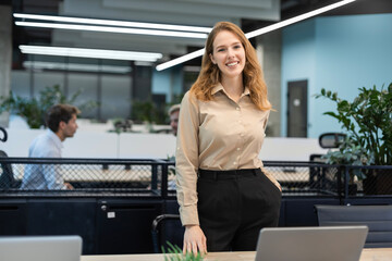 Attractive young businesswoman standing on the table, looking at camera with colleagues on the background