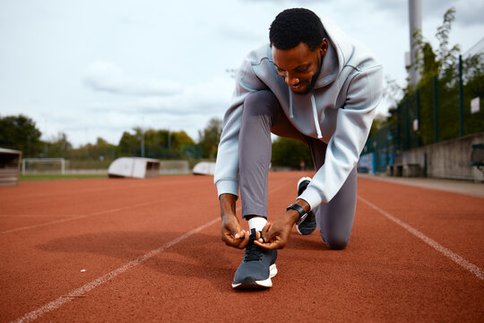 Male athlete tying shoelaces on running track preparing for workout - Powered by Adobe