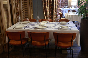 Cozy restaurant dining room with elegant table setting, vintage chandeliers and warm atmosphere. Stylish interior with white tablecloths, soft lighting and retro design details.