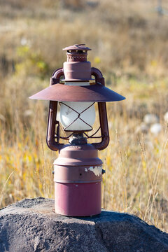 oldschool old red oil lamp sitting on a rock in front of long grass