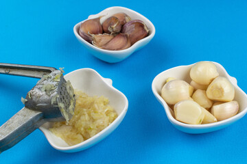 Fresh Garlic Cloves with Garlic Press on Blue Background
