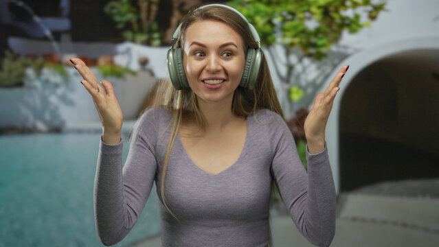 Young woman wearing headphones shows surprise in an outdoor resort pool setting, capturing a fun and joyful moment.