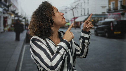 Woman pointing finger on busy city street lined with shops and parked vehicles near sidewalk under...