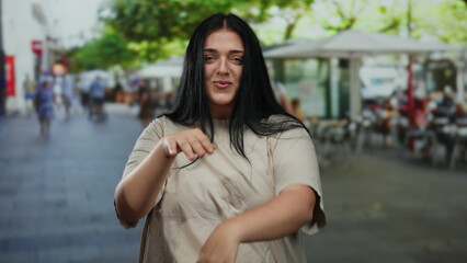 Young plus size woman joyfully dancing with a smile on a lively city street filled with outdoor cafes and trees, showcasing her curvy beauty in a bustling urban environment.