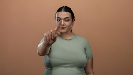 Woman gesturing no with finger on a brown background, capturing a confident young plus size woman's...