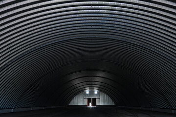 Inside a large empty metal arched hangar. Metal arches form the frame of the hangar.