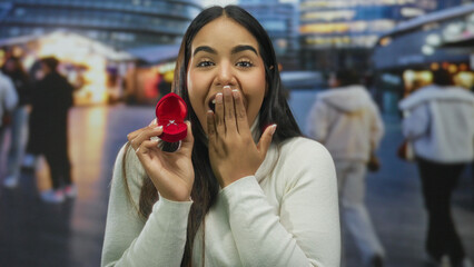 Woman smiling with engagement ring in red box on street evening lights city background facial...