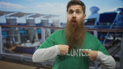 Fototapeta premium Man with long beard points finger to volunteer shirt on cruise deck while opening mouth in surprise; service community support pride.